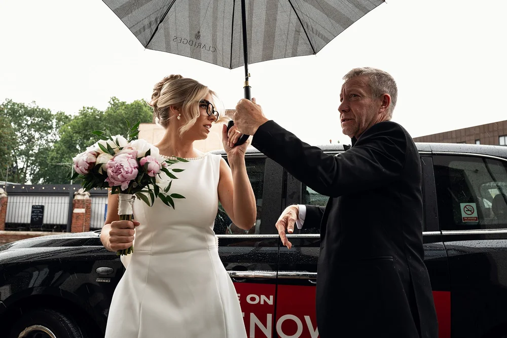 Charley arriving in the rain under an umbrella before the ceremony