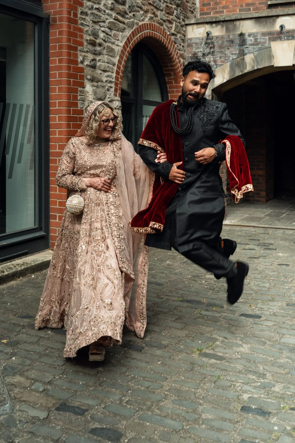Bride and groom running along a cobbled street, her family following behind