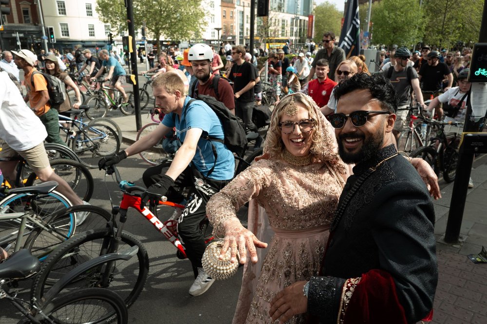 Bride and groom laughing in the middle of a crowd of cyclists on a city street