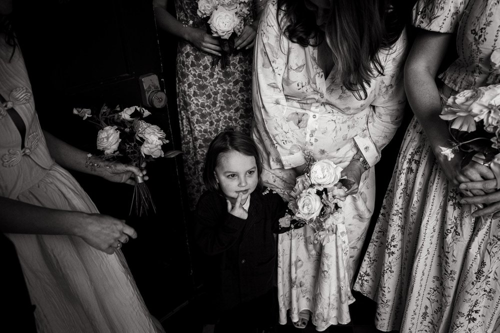 A small flower girl looking up from among the bridesmaids and their bouquets