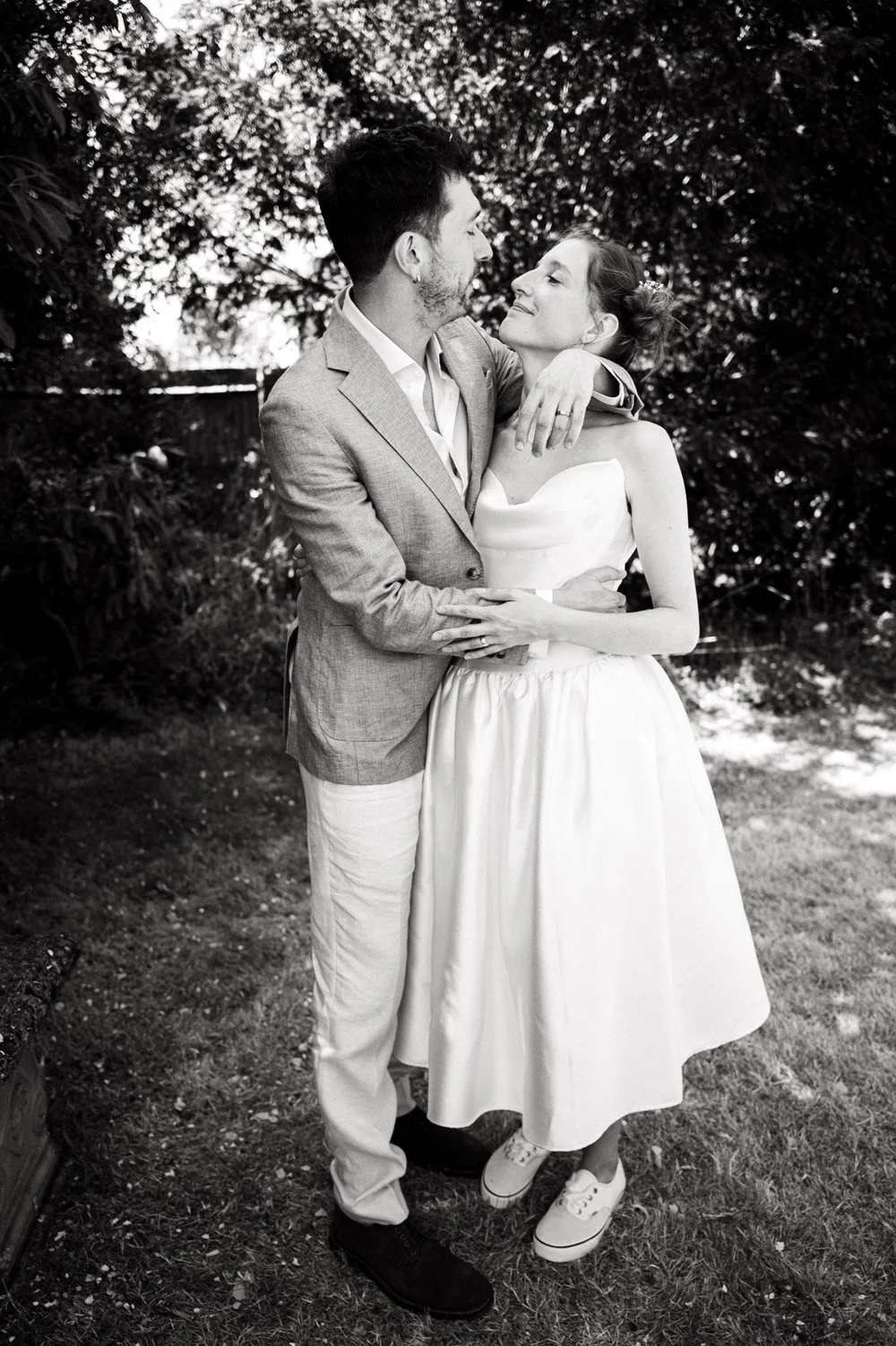 Bride and groom holding each other in dappled light under a tree
