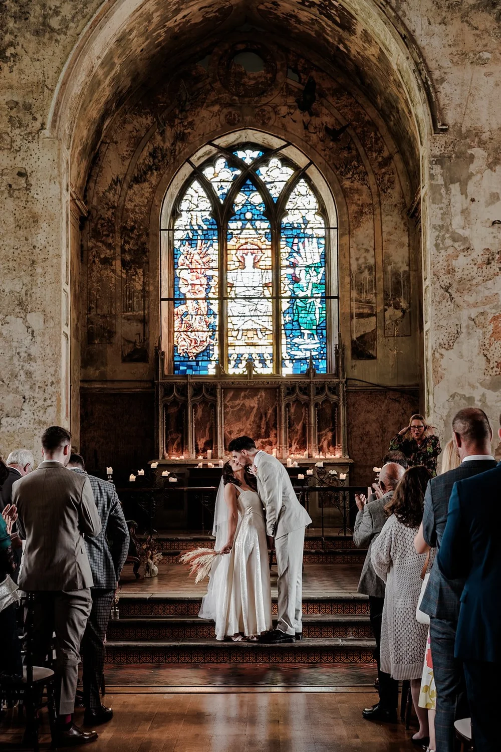 Bride and groom at the altar beneath a stained glass window in a candlelit church