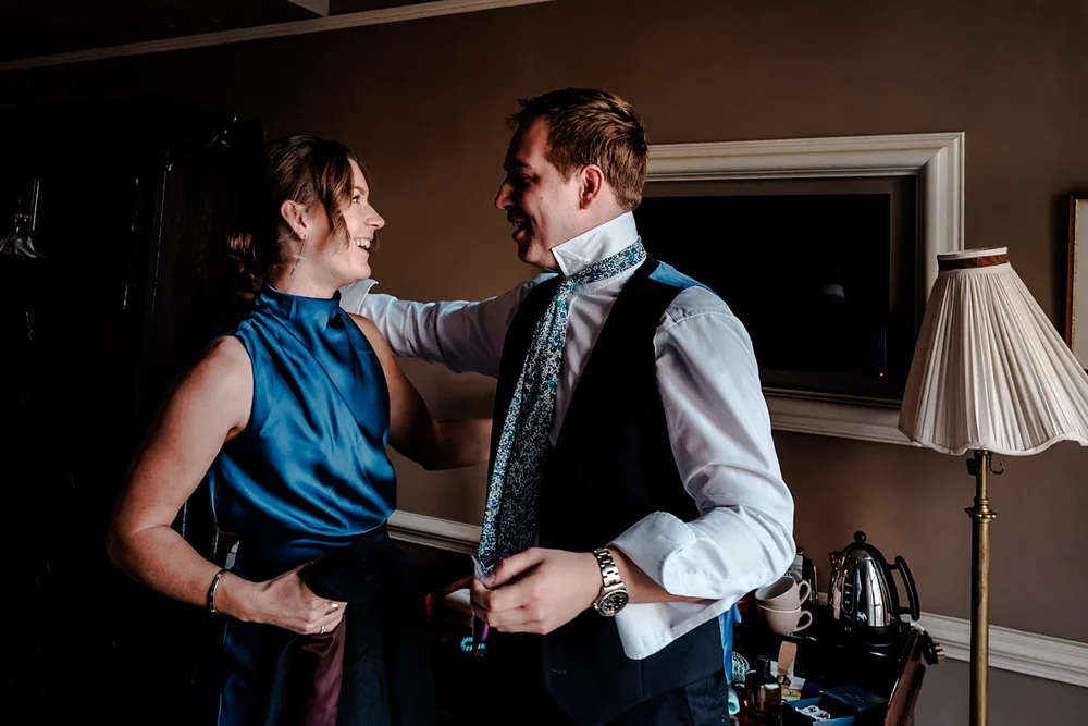 A guest helping the groom with his waistcoat before the ceremony