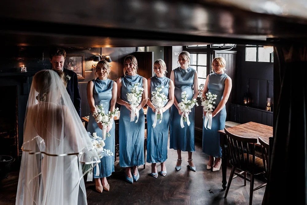Bride in her veil with her bridesmaids in blue holding bouquets