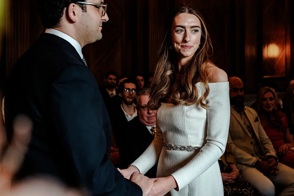 Bride and groom holding hands during their ceremony in a panelled room