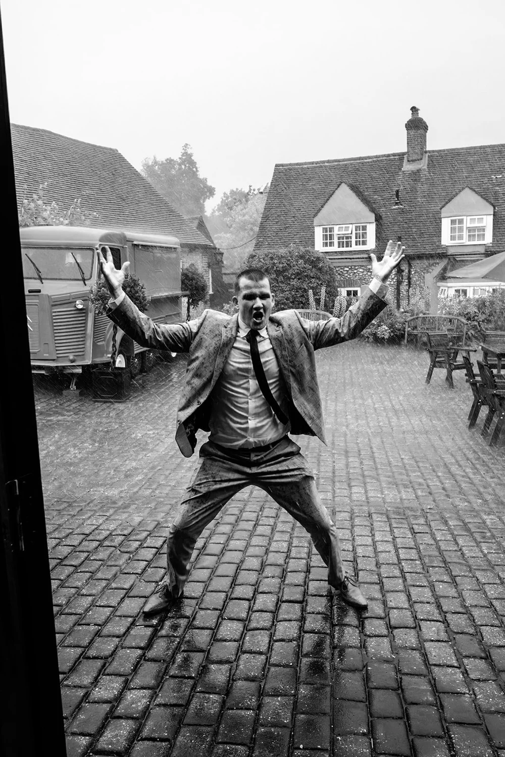 Groom leaping into the air in a rainy cobbled courtyard