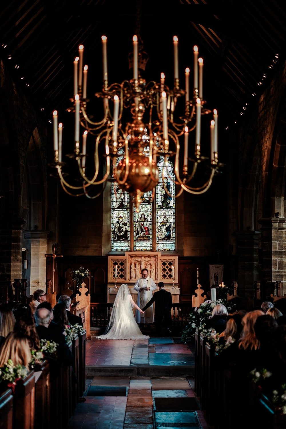 Bride walking down the aisle beneath a candlelit chandelier