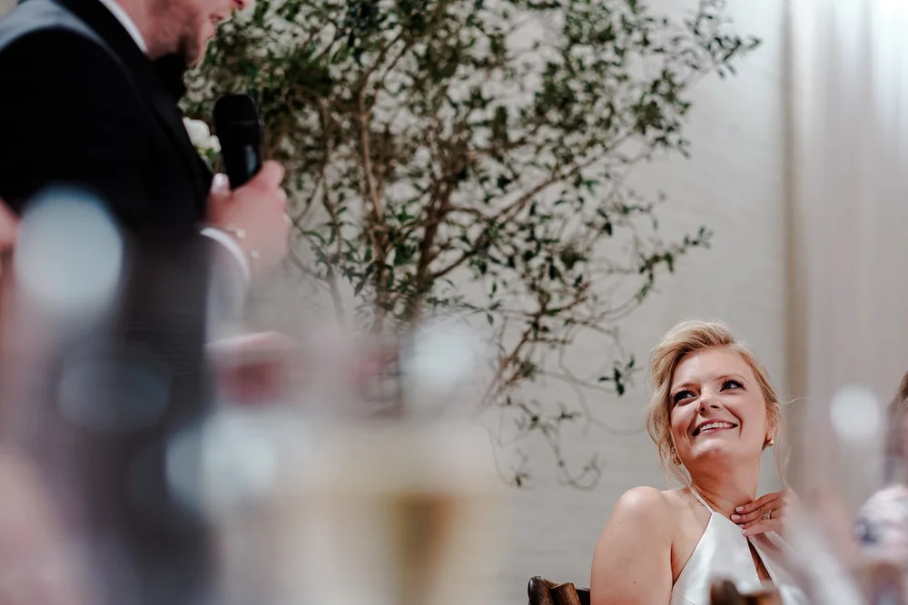 A guest laughing during the drinks reception, framed by an olive tree
