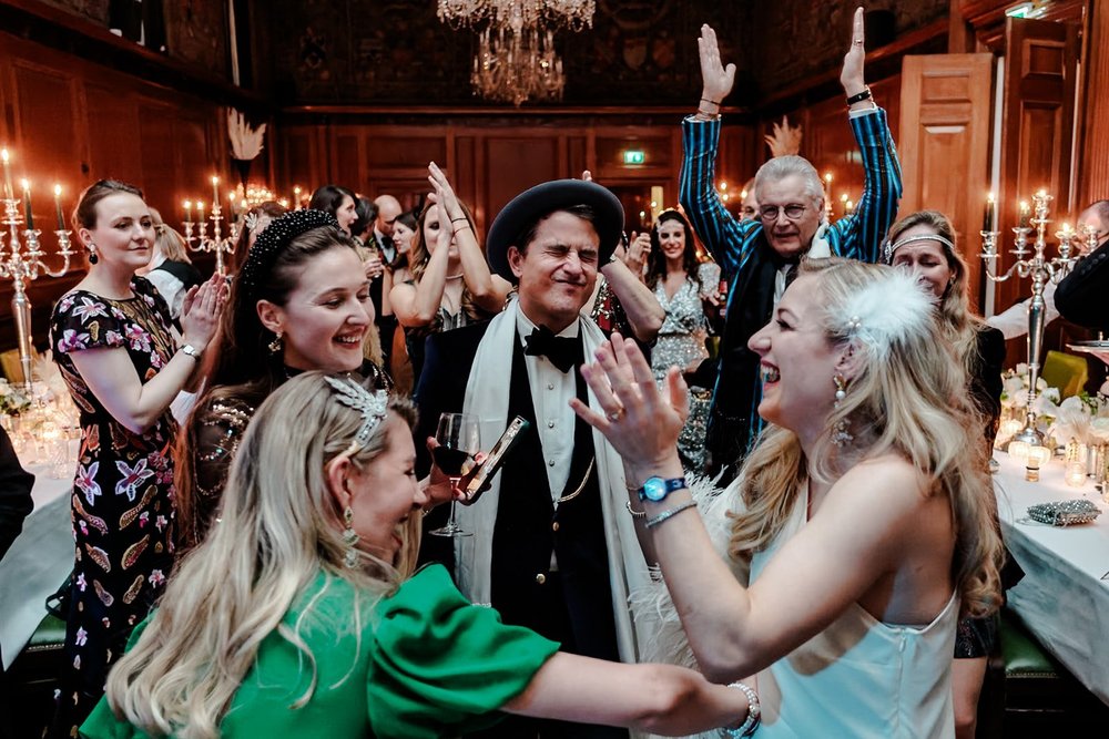 Guests cheering with arms raised at a candlelit wedding breakfast