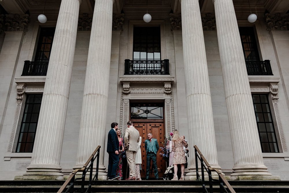 Bride and groom dwarfed by the columns of a grand town hall entrance