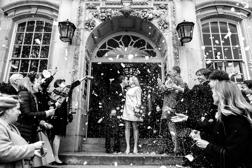 Bride and groom kissing in a confetti shower in a stone doorway