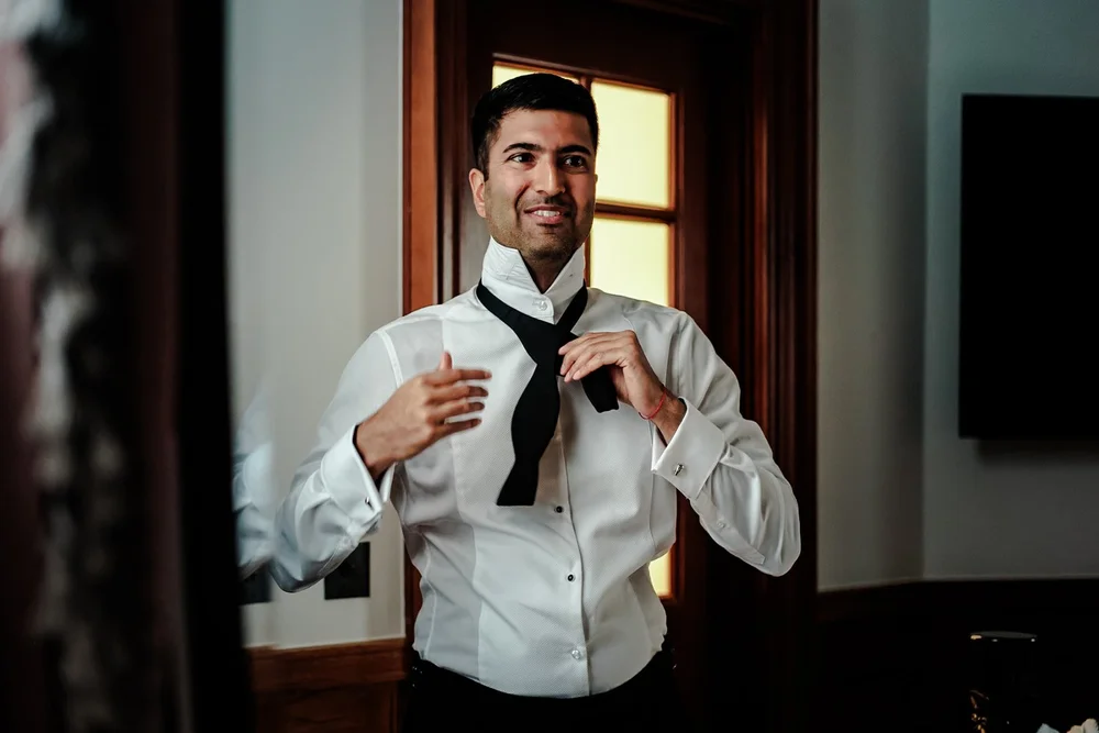 Groom fastening his bow tie by a window