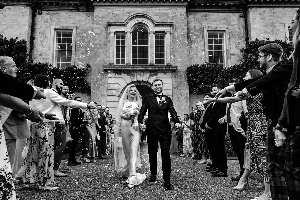 Bride and groom walking through a confetti tunnel outside a country house