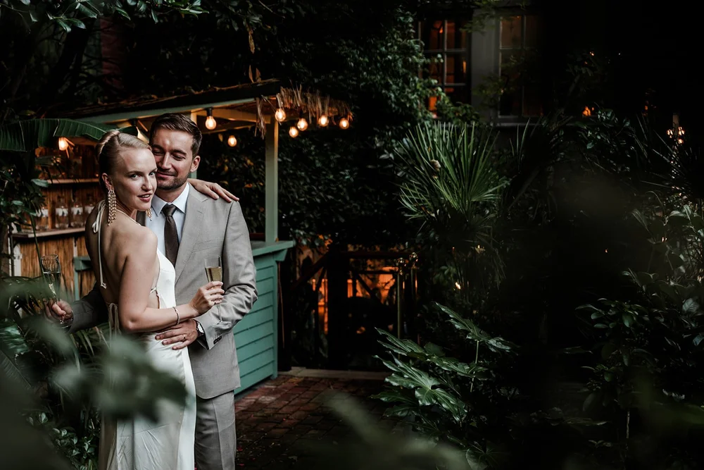 Bride and groom embracing in a plant filled bar under festoon lights