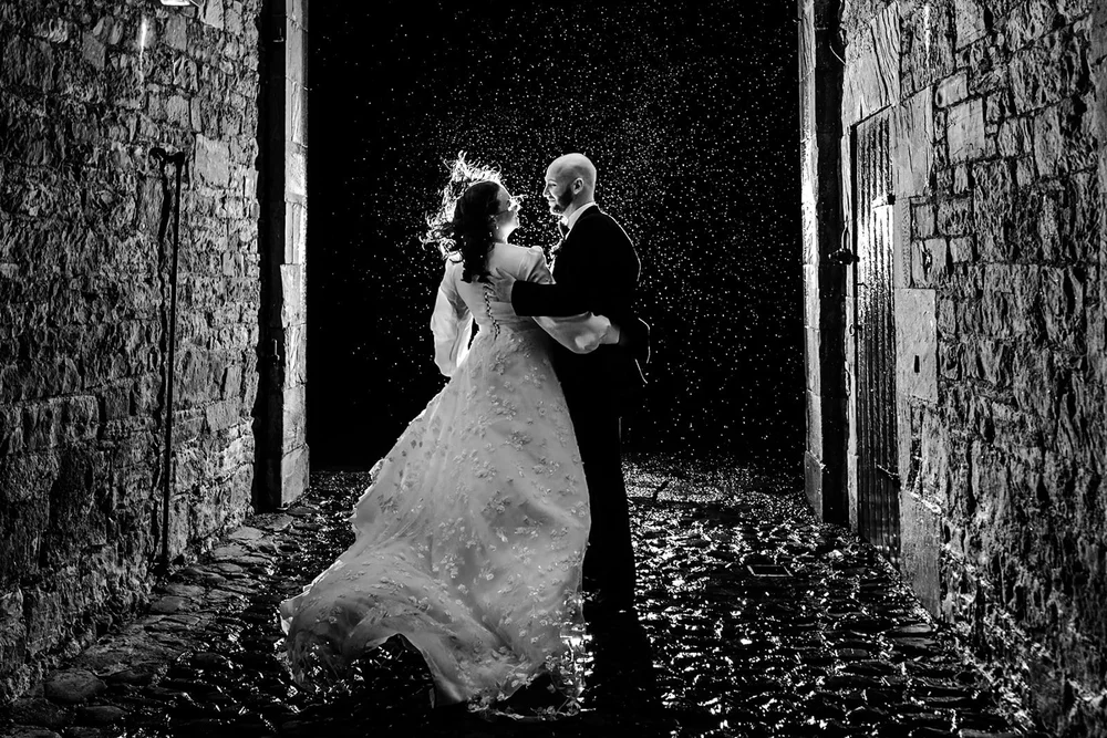 Bride and groom dancing in a stone passage as confetti falls around them