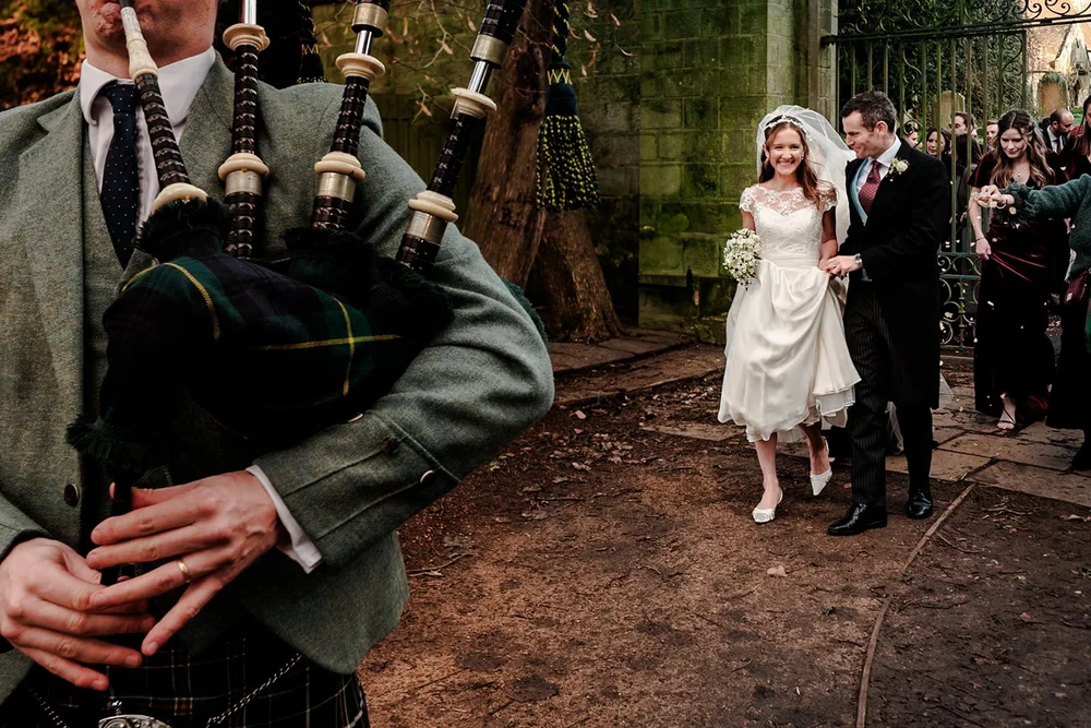 A piper leading the bride and groom out through the gates