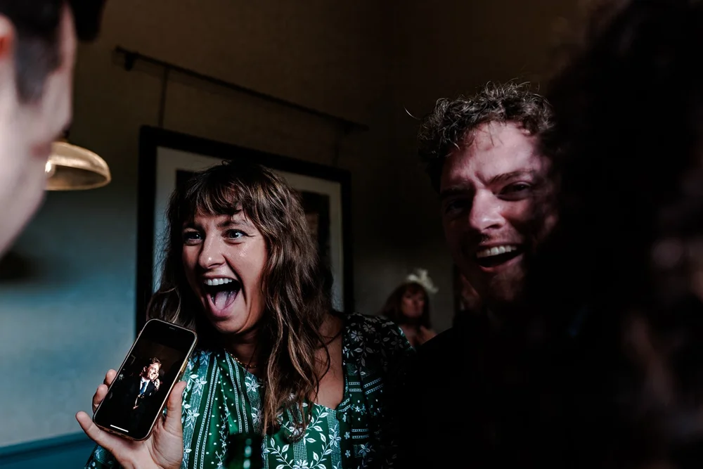 Guests laughing as they hold up a phone to include an absent friend