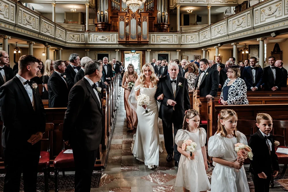 Bride walking down the aisle with her father, flower girls following behind