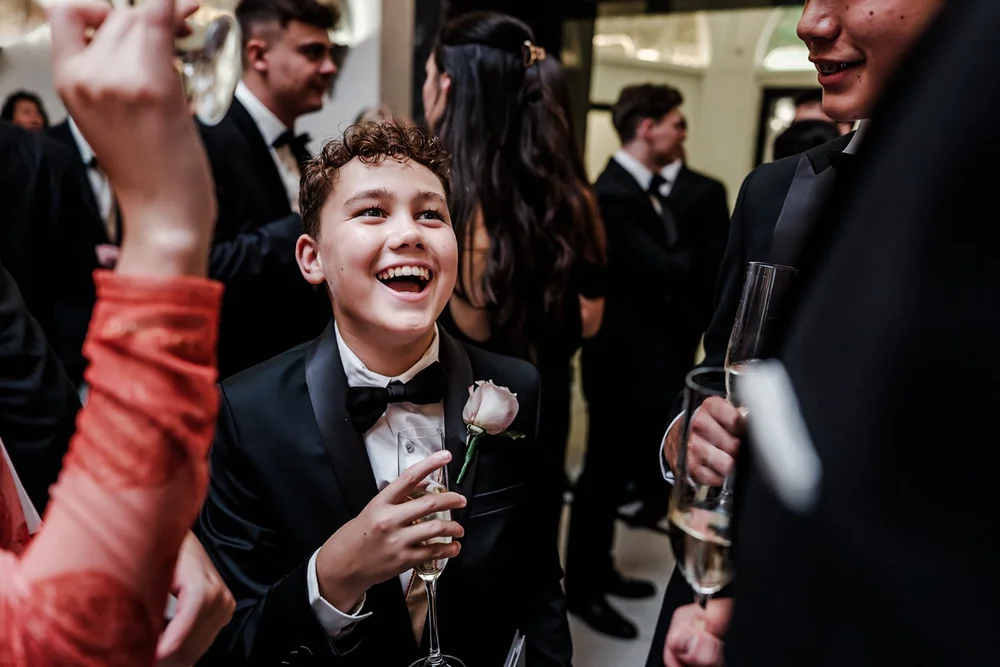 A young guest in black tie laughing with a rose and a glass of champagne