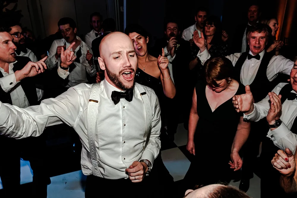Groom leading the crowd on the dance floor with his arms outstretched