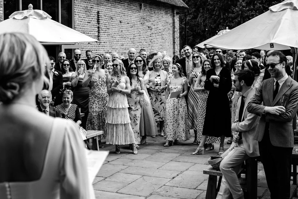 Guests gathered outdoors under umbrellas watching the couple