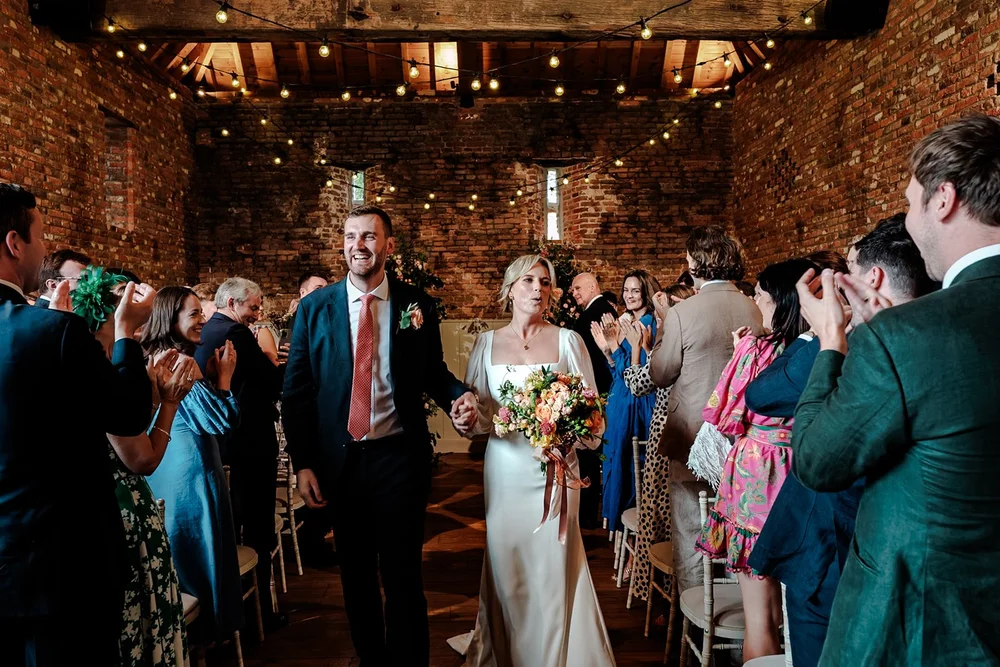 Bride and groom walking back up the aisle of a brick barn