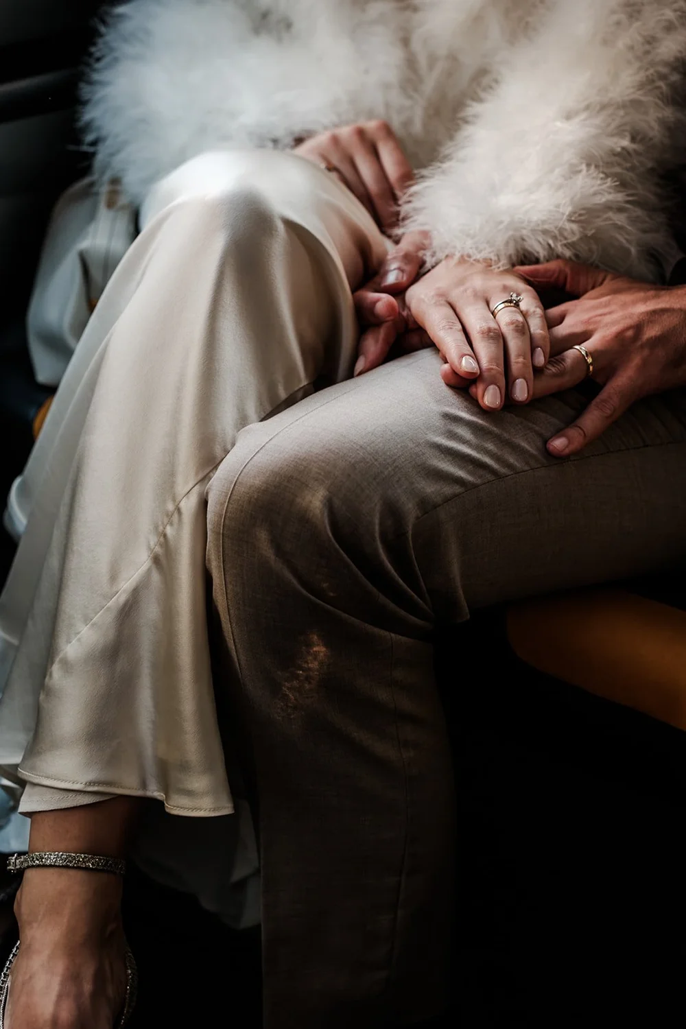 The couple&rsquo;s hands resting together, satin dress and fur wrap