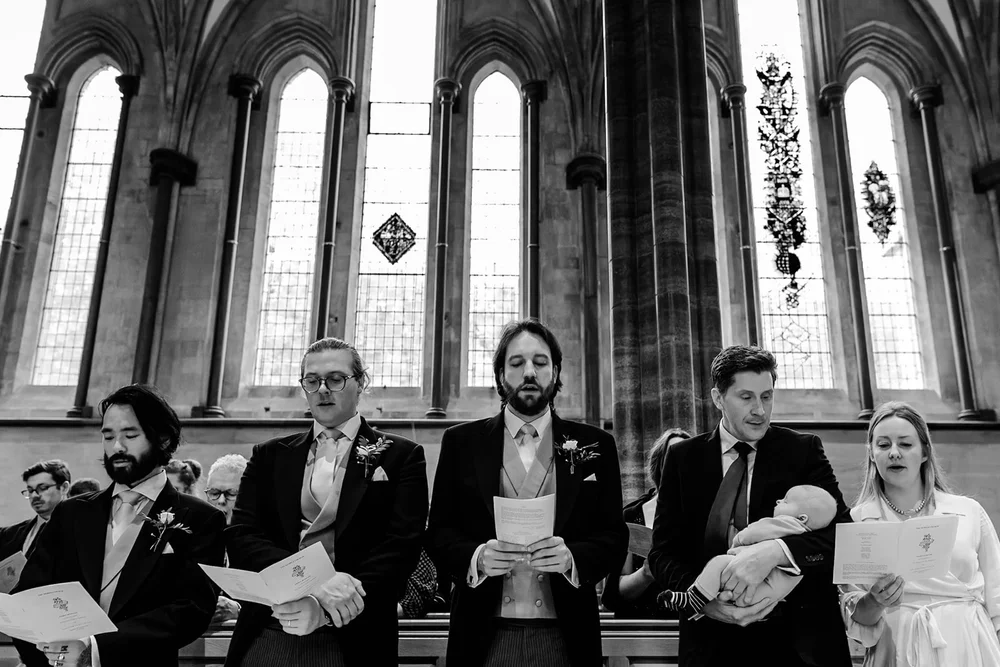 Guests singing from hymn sheets beneath gothic church windows