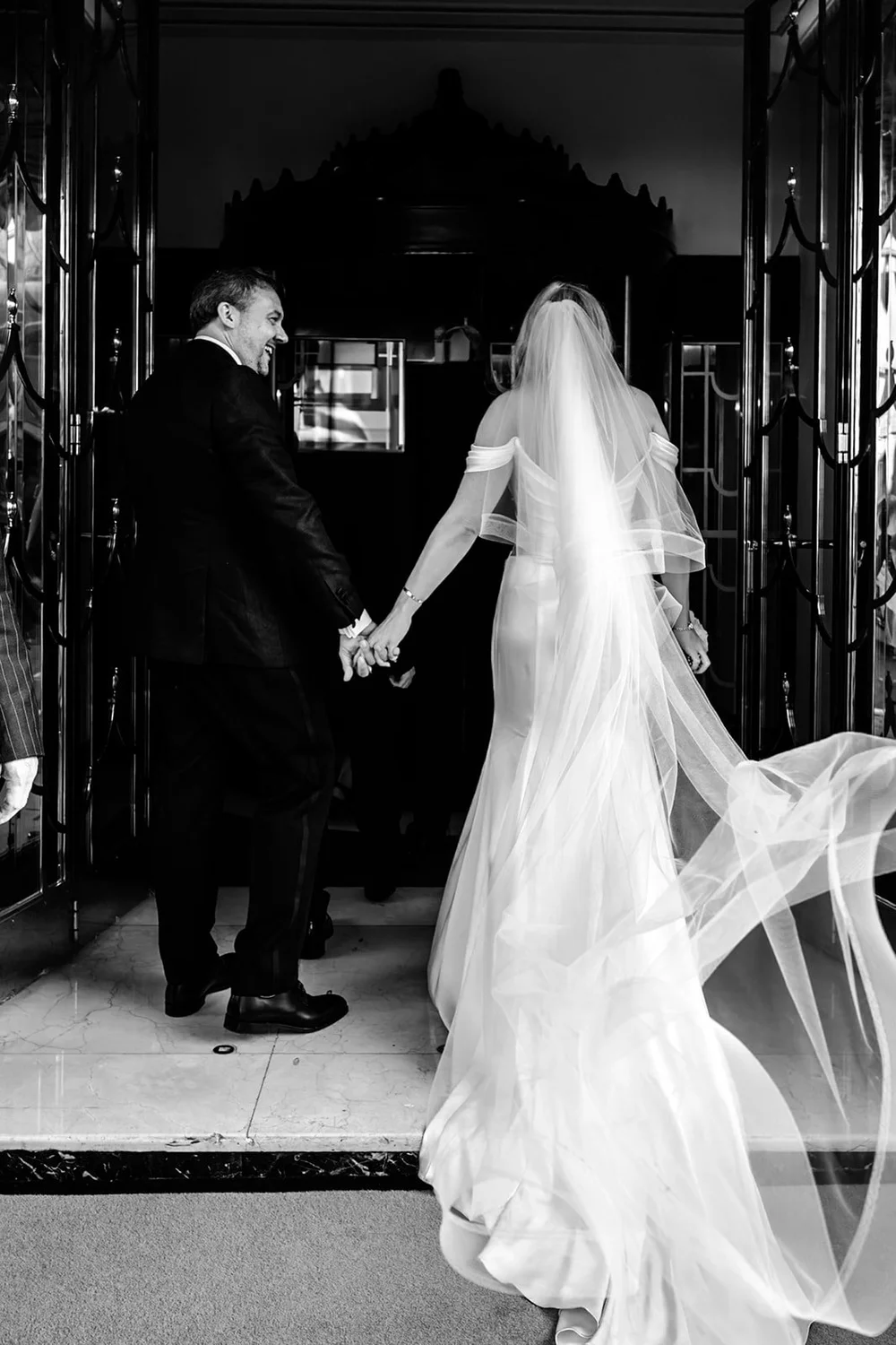 The bride&rsquo;s veil flowing behind her as the couple walk out