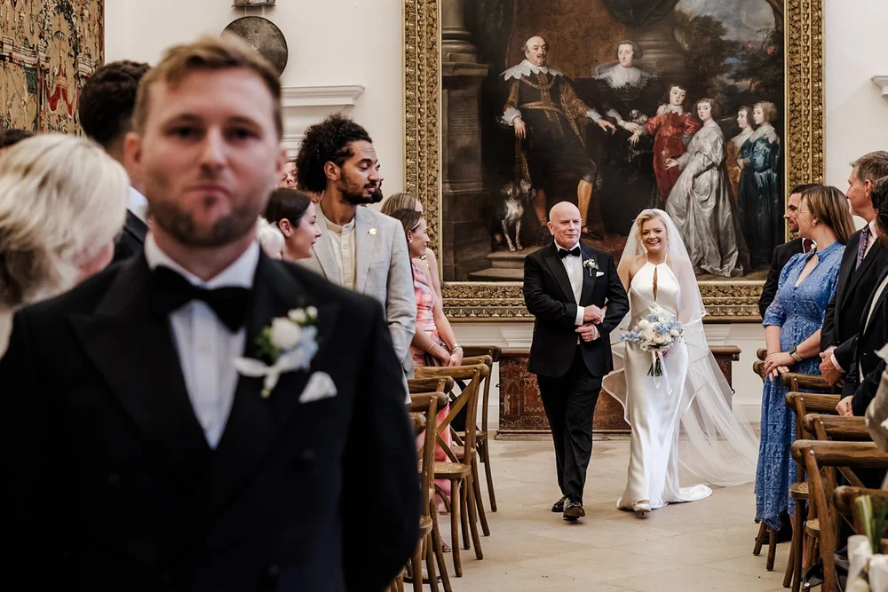 Groom watching his bride enter beneath a grand portrait