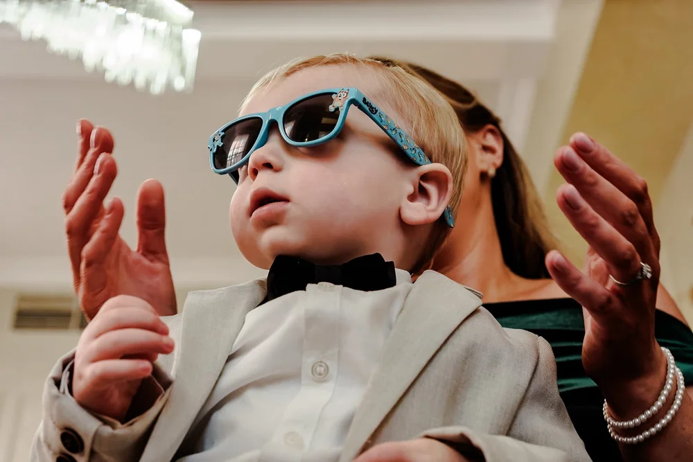 A young guest in sunglasses and a bow tie clapping during the ceremony