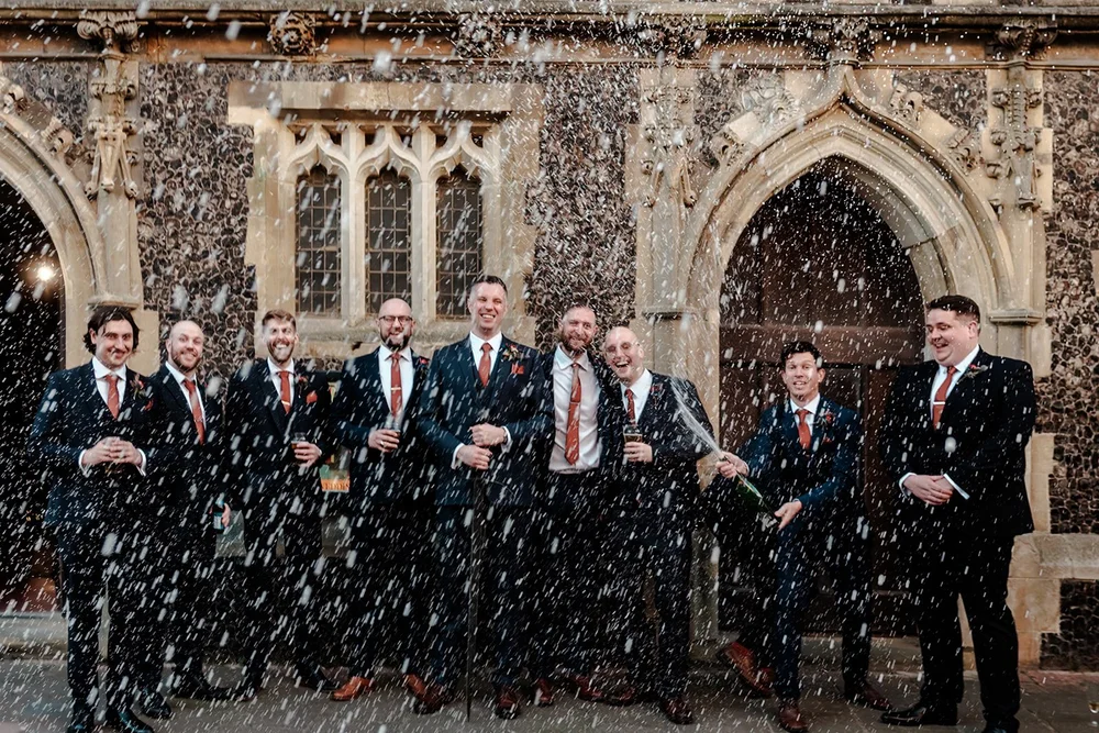 Groomsmen spraying champagne outside a stone church