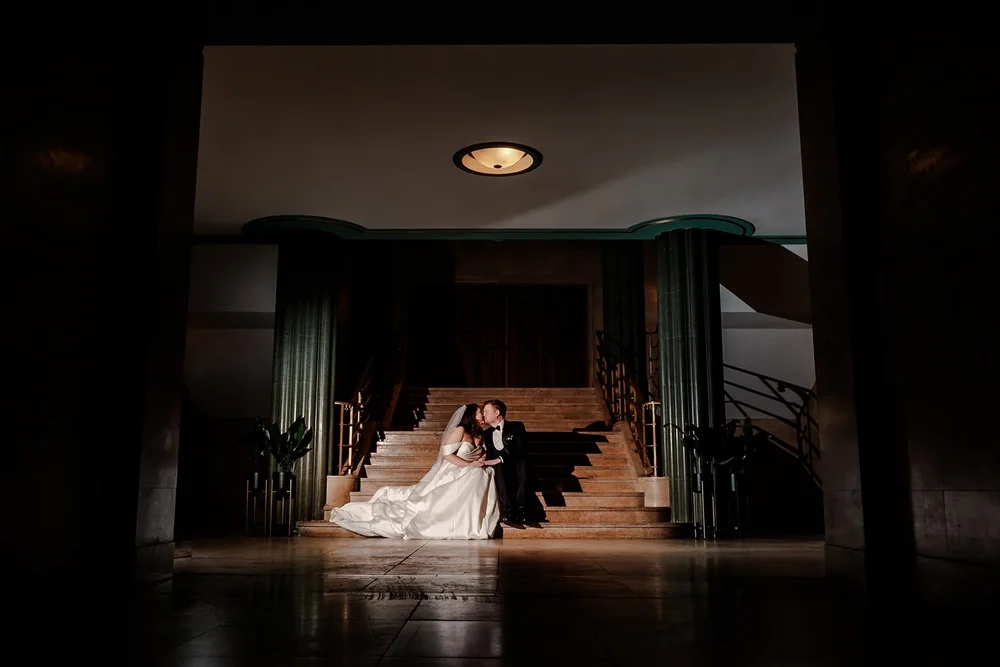 Bride sitting alone on a lit staircase in a darkened room