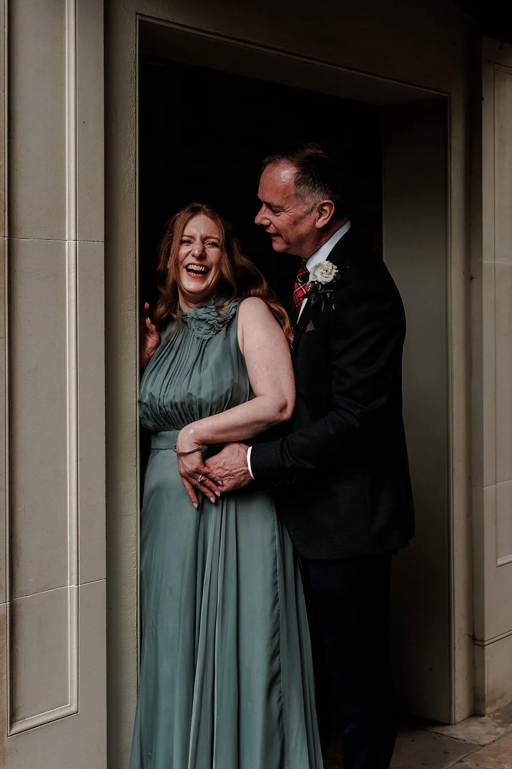 The bride&rsquo;s parents laughing together in a doorway