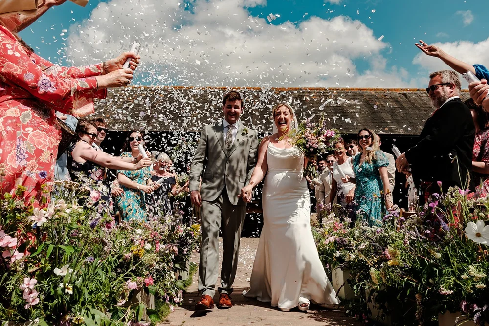 Bride and groom walking through a confetti shower on a bright summer day