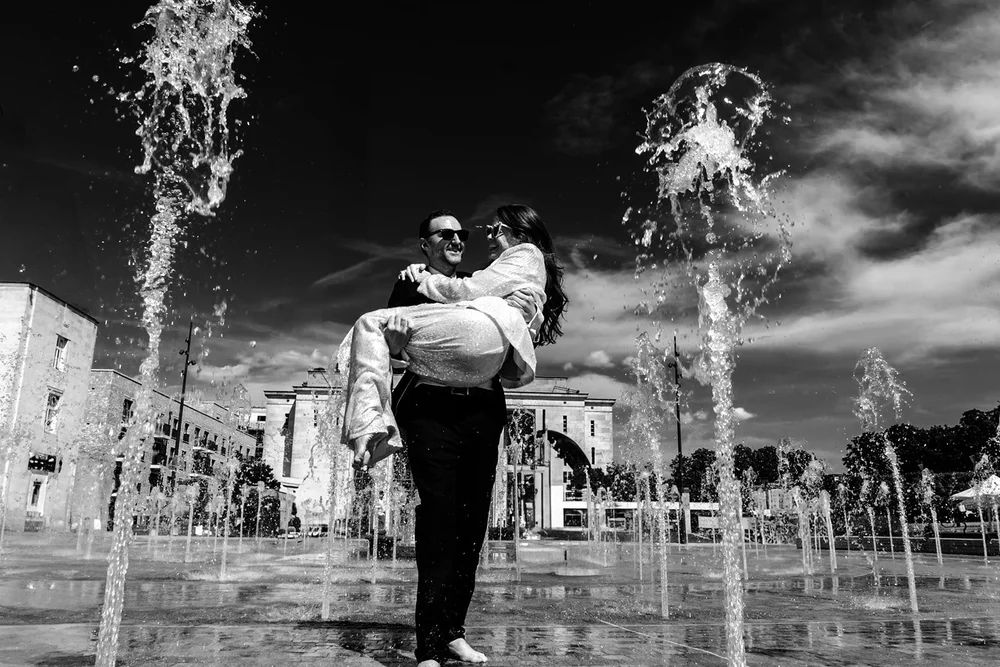 Groom lifting the bride between fountains on a sunny day