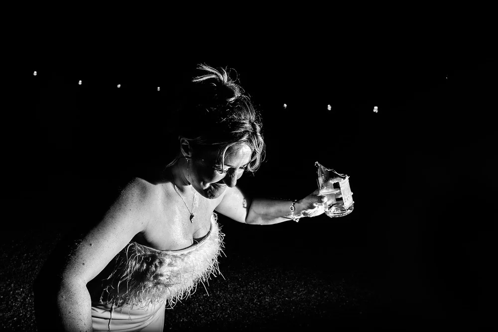 Bride reaching out with a drink in the dark of the evening party