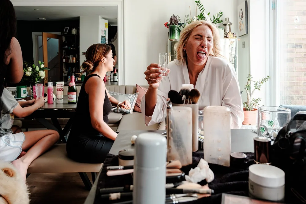 Bride laughing with a glass of champagne as she gets ready with her bridesmaids