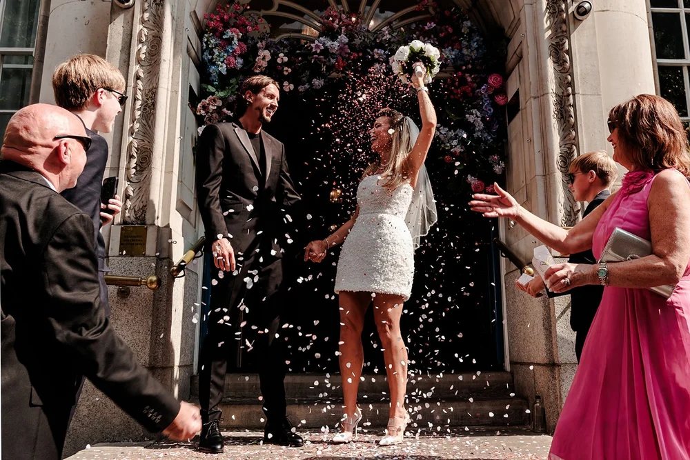 Bride throwing her bouquet in the air on the steps in a confetti shower