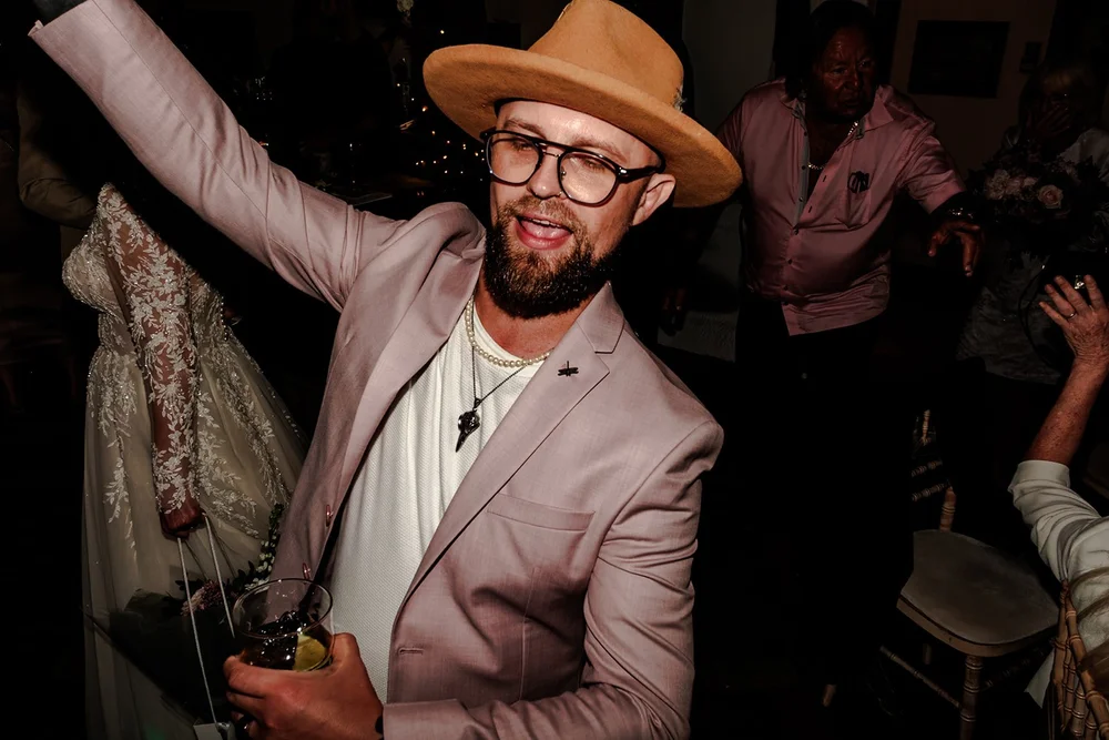 A guest in a pink suit and hat dancing with his arm in the air