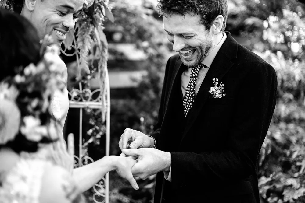 Groom laughing as he puts the ring on the bride&rsquo;s finger