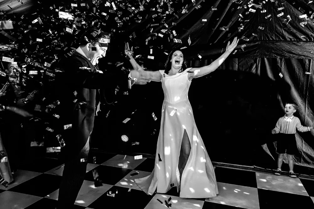 Bride standing with her arms outstretched in a shower of confetti