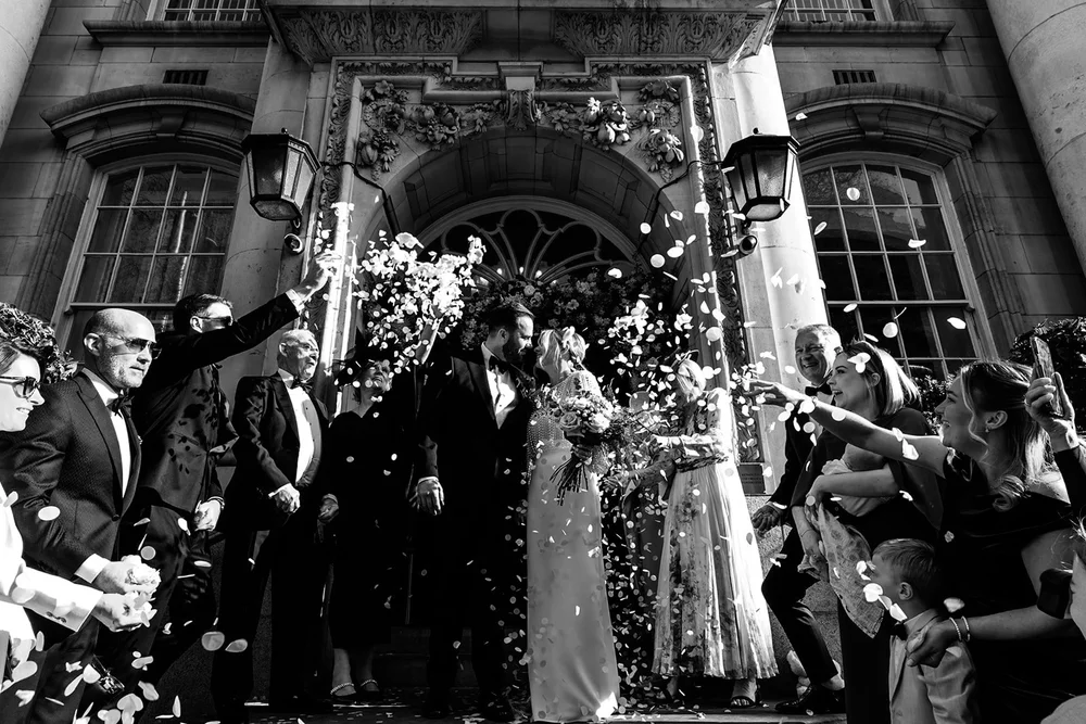 Bride and groom in a confetti shower outside a grand entrance at night