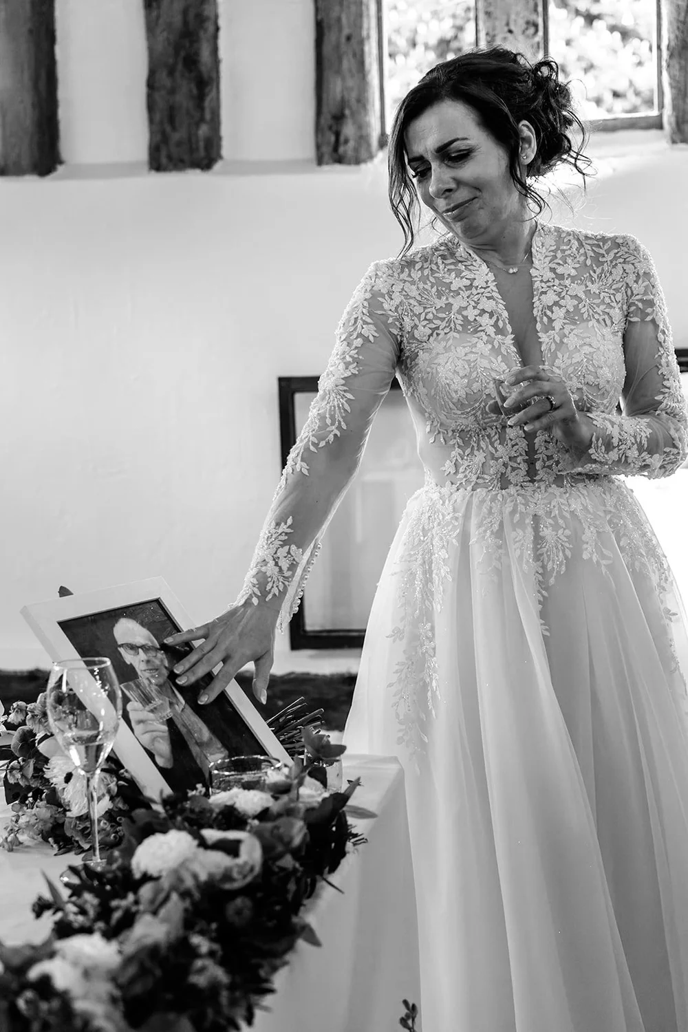 Bride pausing beside a framed photograph of a loved one who could not be there