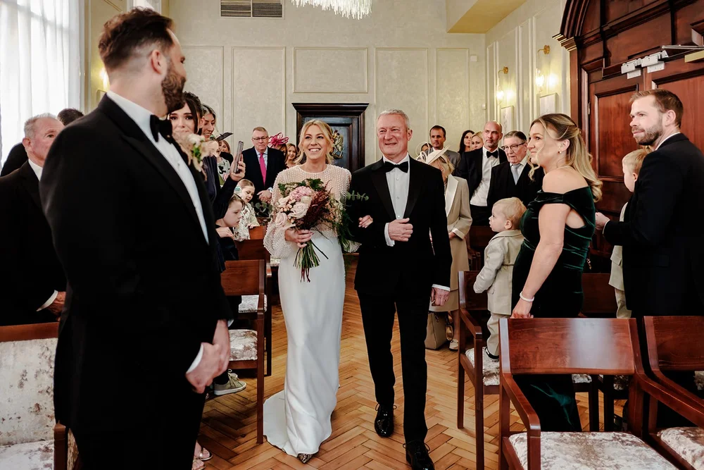 Bride walking down the aisle with her father in a panelled ceremony room