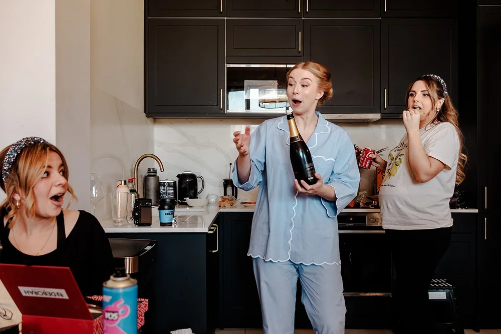 The bride in pyjamas opening champagne in the kitchen on the wedding morning