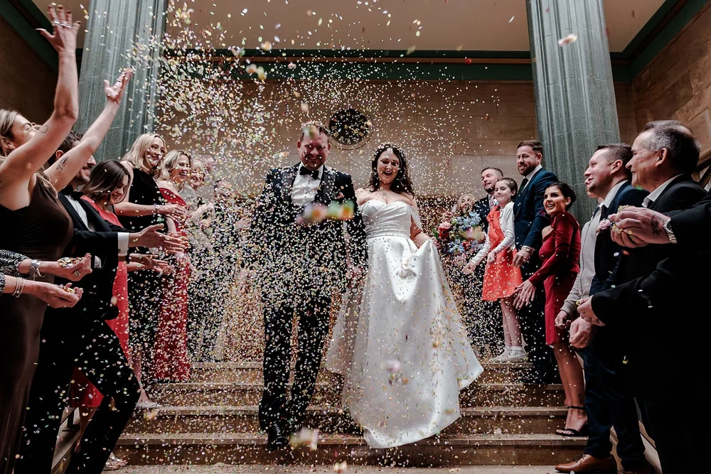 Bride and groom walking down the steps through a huge confetti shower