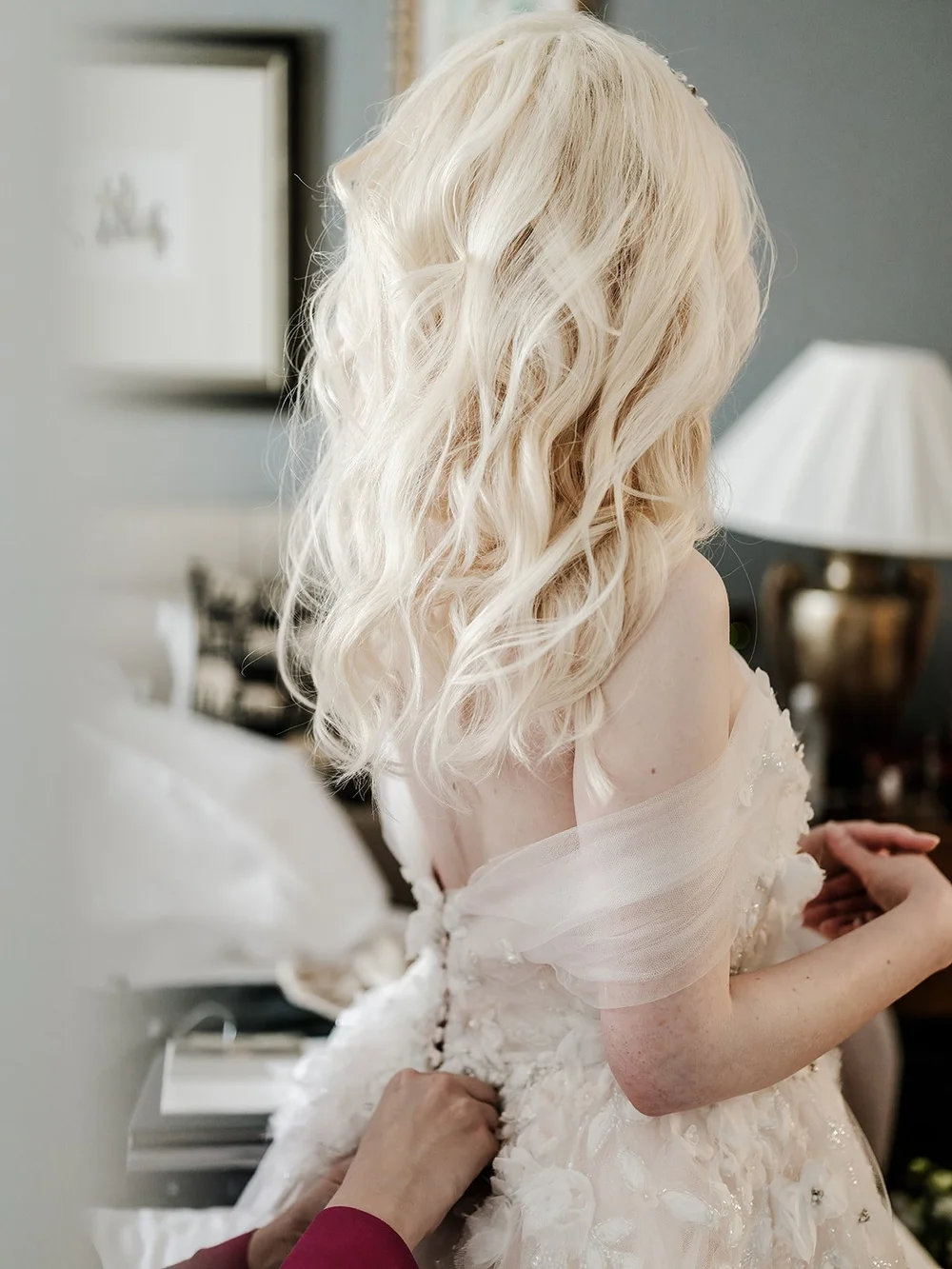 The back of the bride&rsquo;s dress being fastened before she leaves
