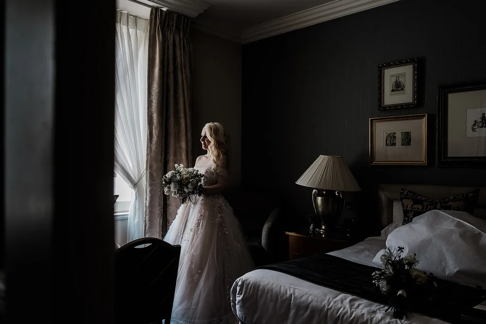 Bride standing at the window of a dark panelled room in her dress