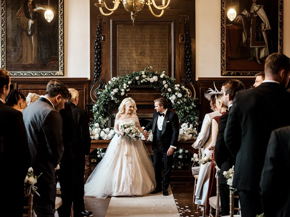 Bride and groom at the flower arch as their guests look on